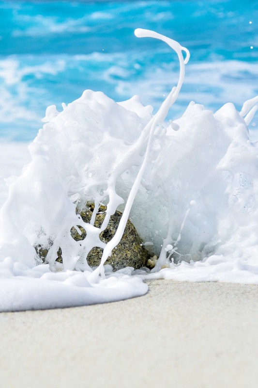 Sea foam breaking over a rock on white sand